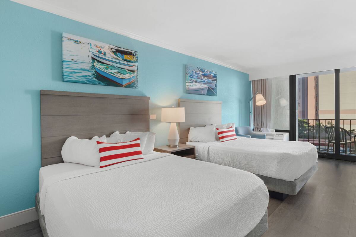 A hotel room with two beds, a large window with a view, and artwork on the walls.