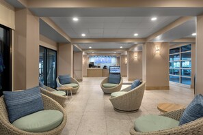 A hotel lobby with wicker chairs, a reception desk, and a view through large windows.