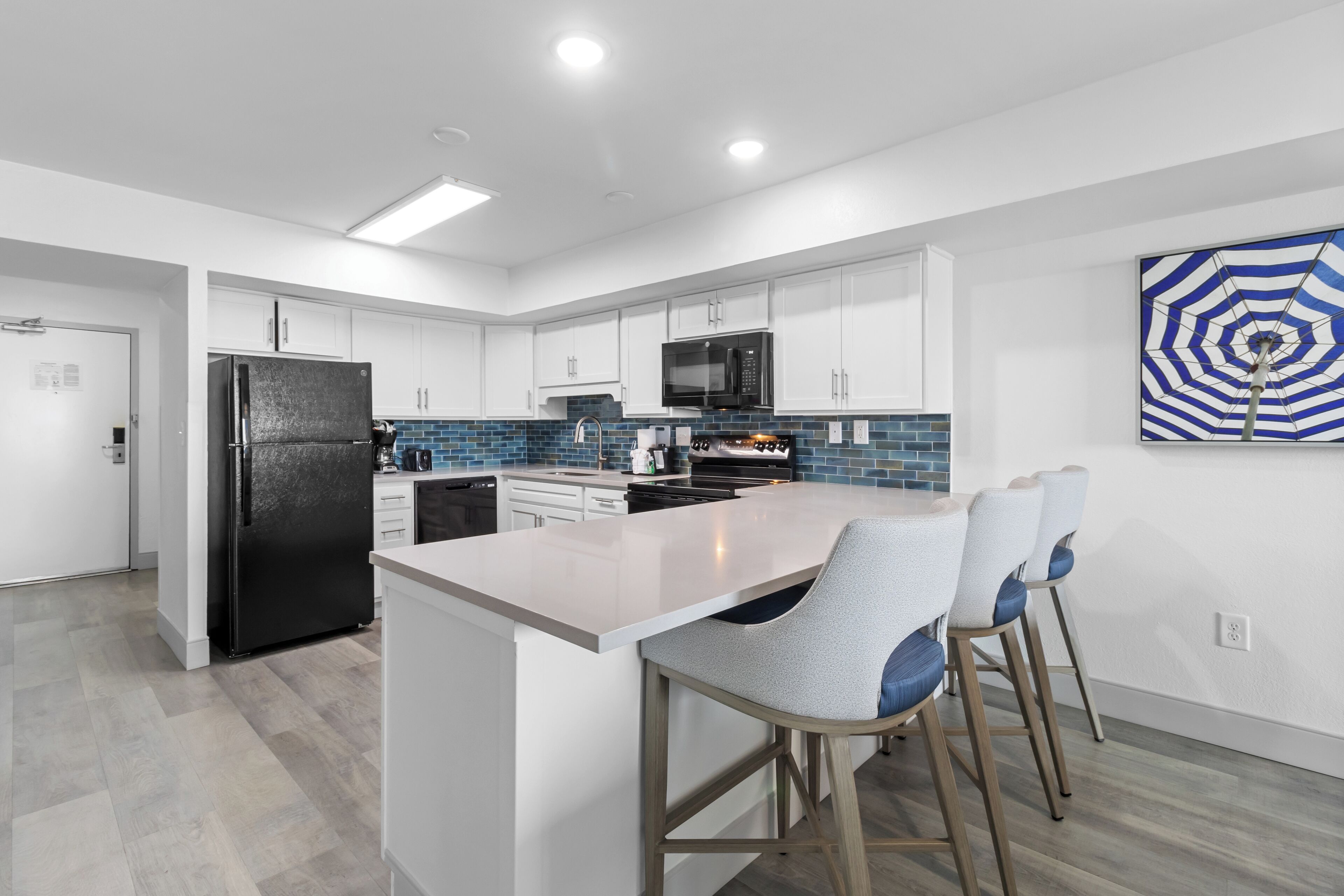 Una cocina moderna con armarios blancos, un refrigerador negro, salpicadero azul y una isla grande con taburetes de bar.
