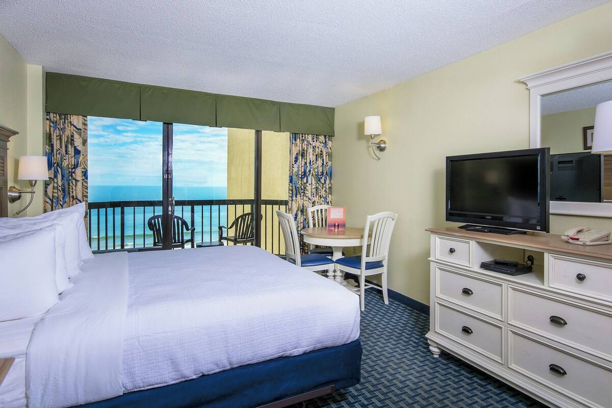 A hotel room with a bed, a desk with a chair, a television, and a dresser.