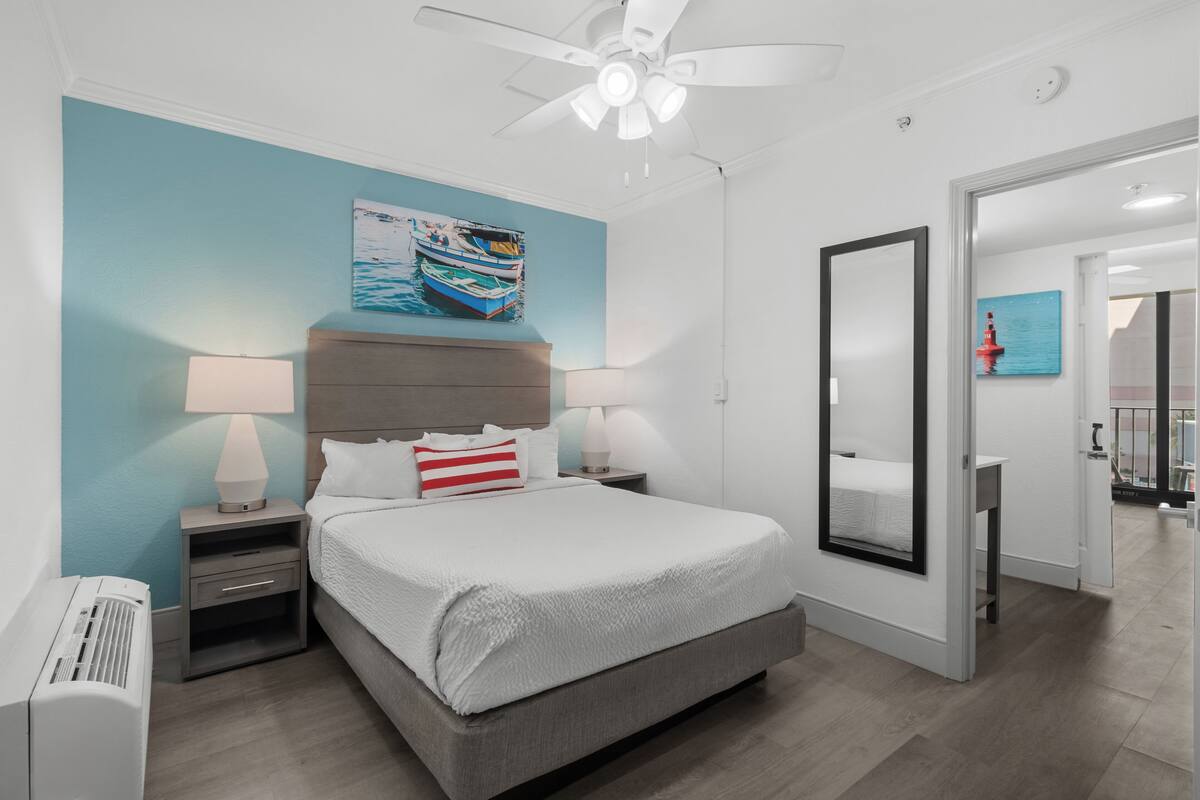 A modern bedroom with a bed, nightstands, a ceiling fan, and artwork on the wall.