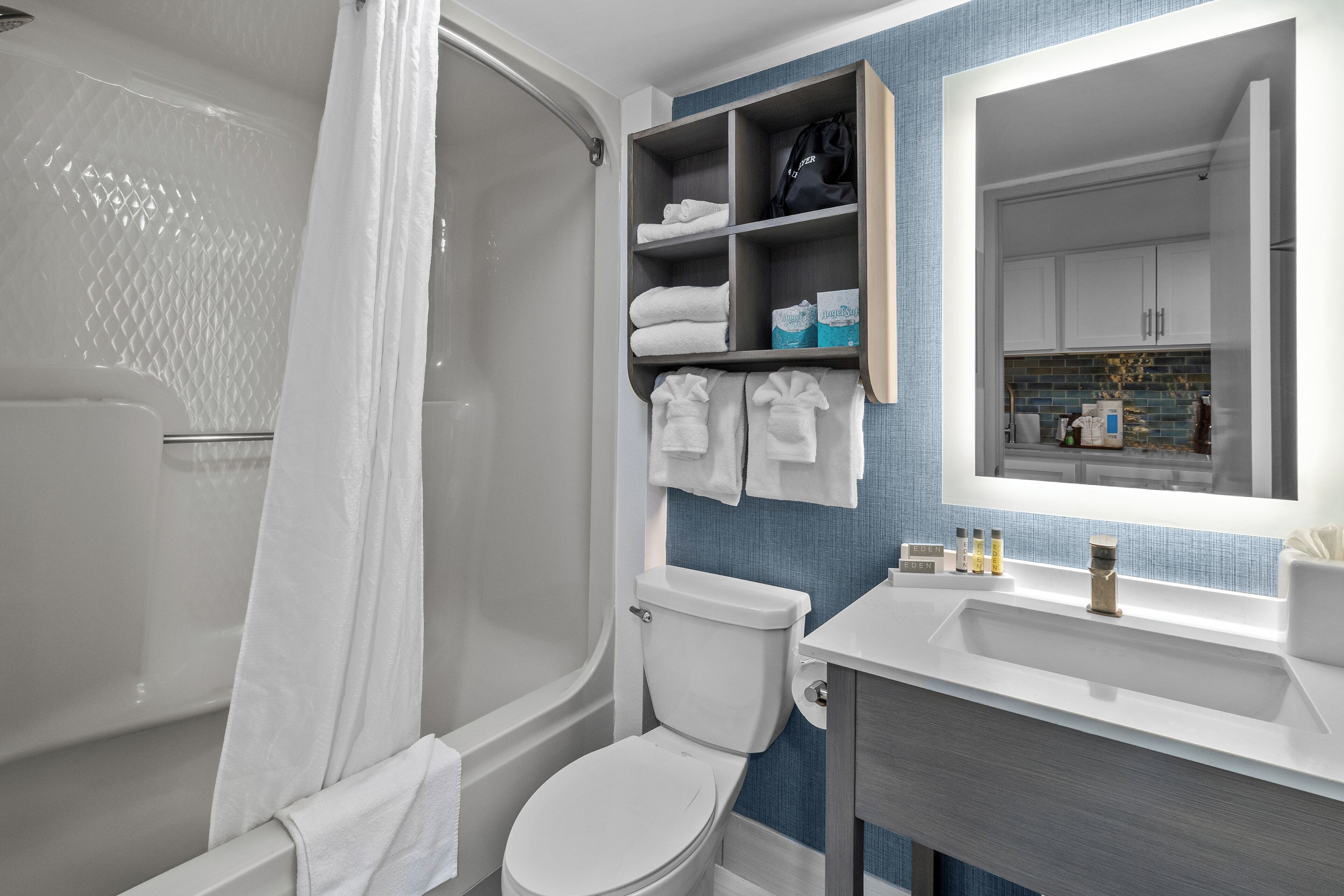 A modern bathroom with a shower, toilet, and sink. There are shelves with towels and toiletries.