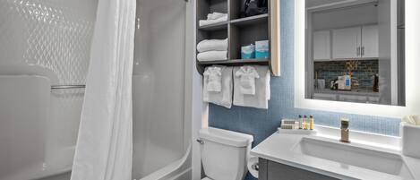 A modern bathroom with a shower, toilet, and sink. There are shelves with towels and toiletries.