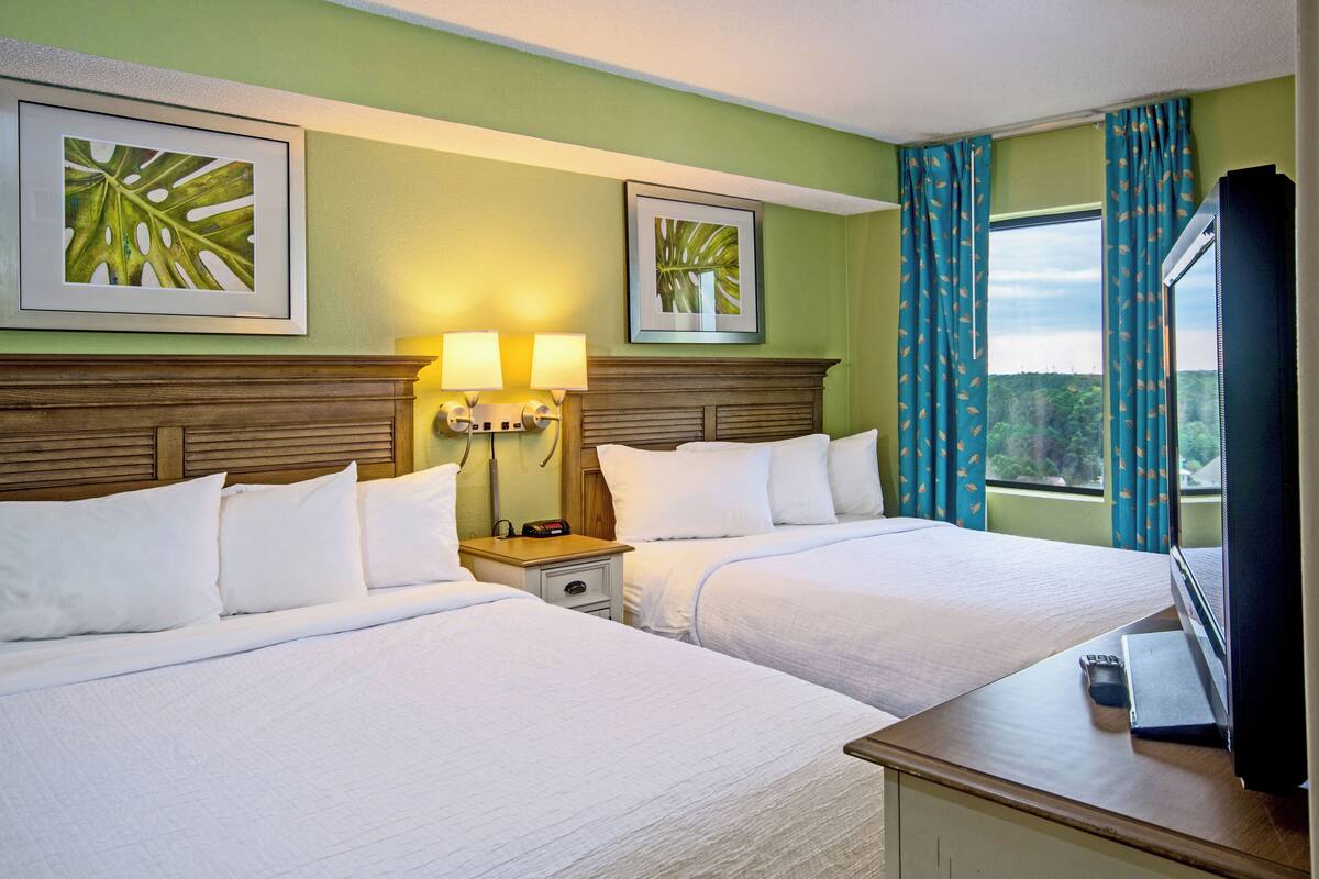 A hotel room with two beds, a nightstand with lamps, and a TV on a dresser.