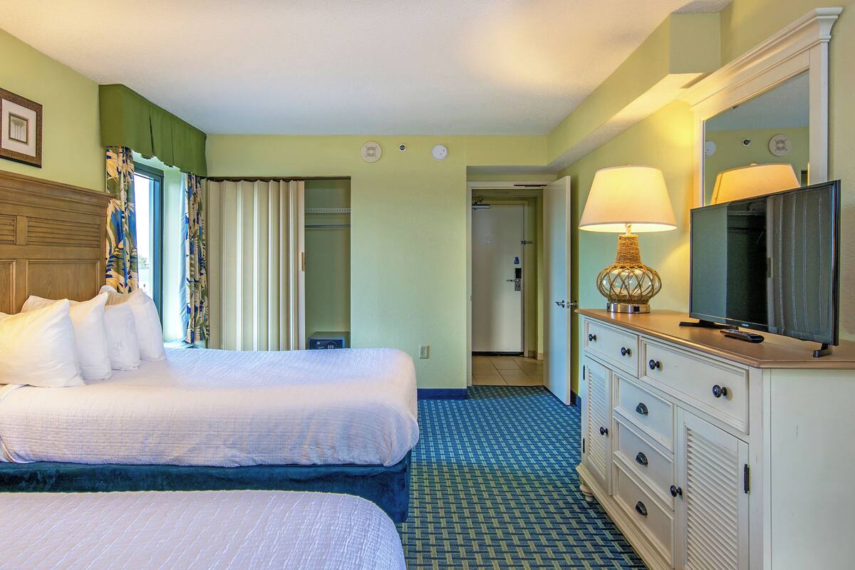 A hotel room with two beds, a television, a dresser, and a bathroom visible through an open door.