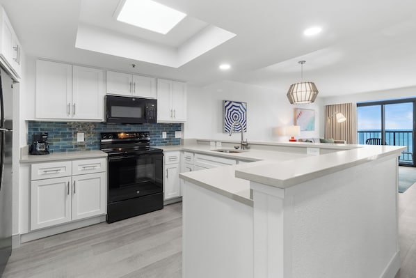 A modern kitchen with white cabinetry, a black oven, and a blue-tiled backsplash. - Compass Cove Resort (Myrtle Beach)