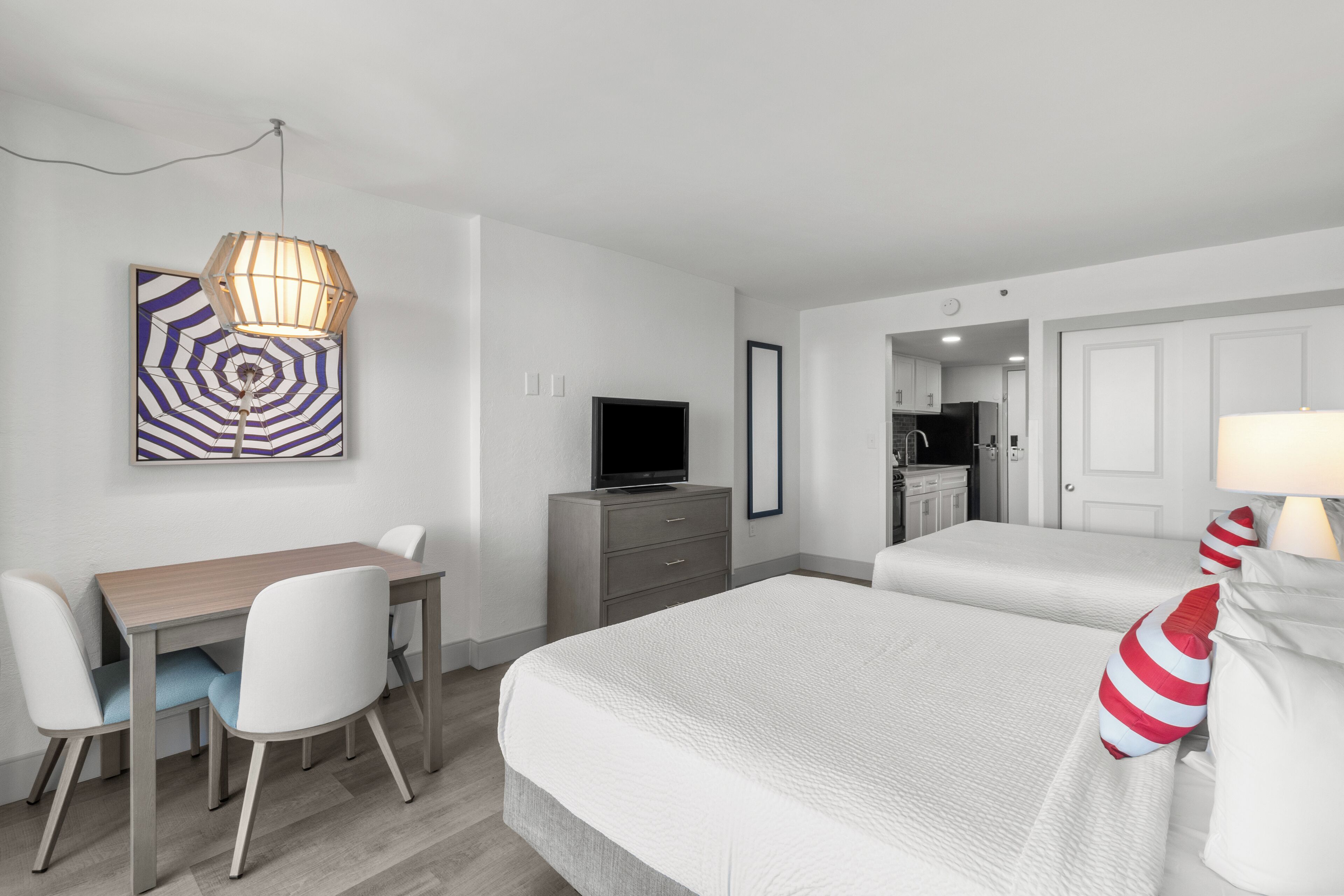 A hotel room with a bed, a desk with chairs, a television, and a painting on the wall.