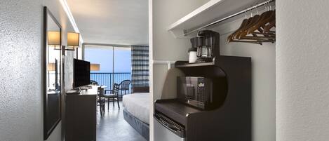 Quarto de hotel com varanda, uma mesa, uma cadeira, uma cama, micro-ondas e máquina de café.