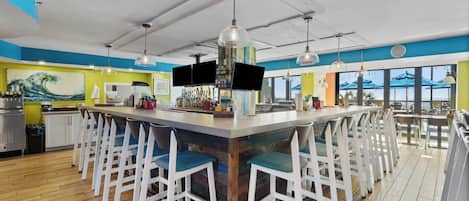 A bar area with a central island, white bar stools, and a large painting on the wall.