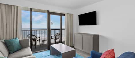 Habitación de hotel con balcón, televisión, sofá, sillón y mesa de centro.
