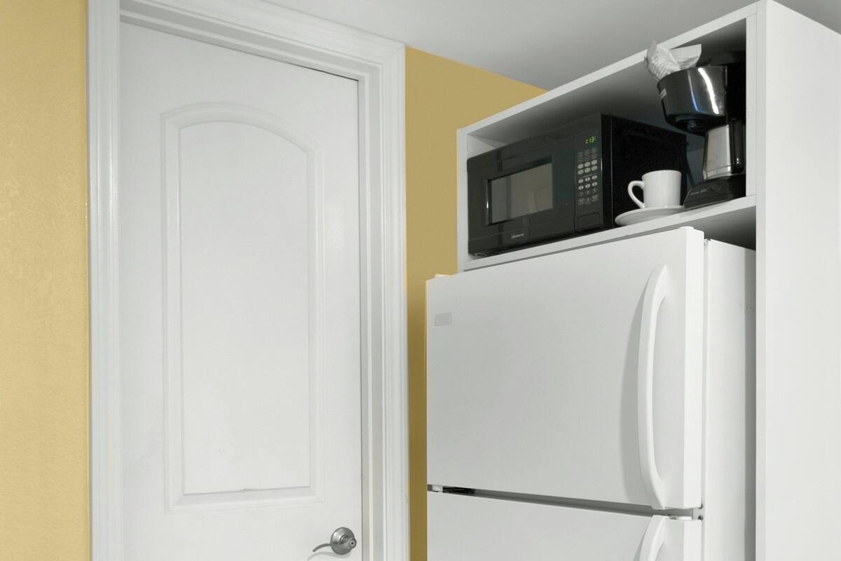 A white refrigerator with a microwave on top, a white door, and a tiled floor.