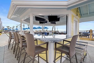 A covered outdoor bar area with a pool table, bar stools, and umbrellas.