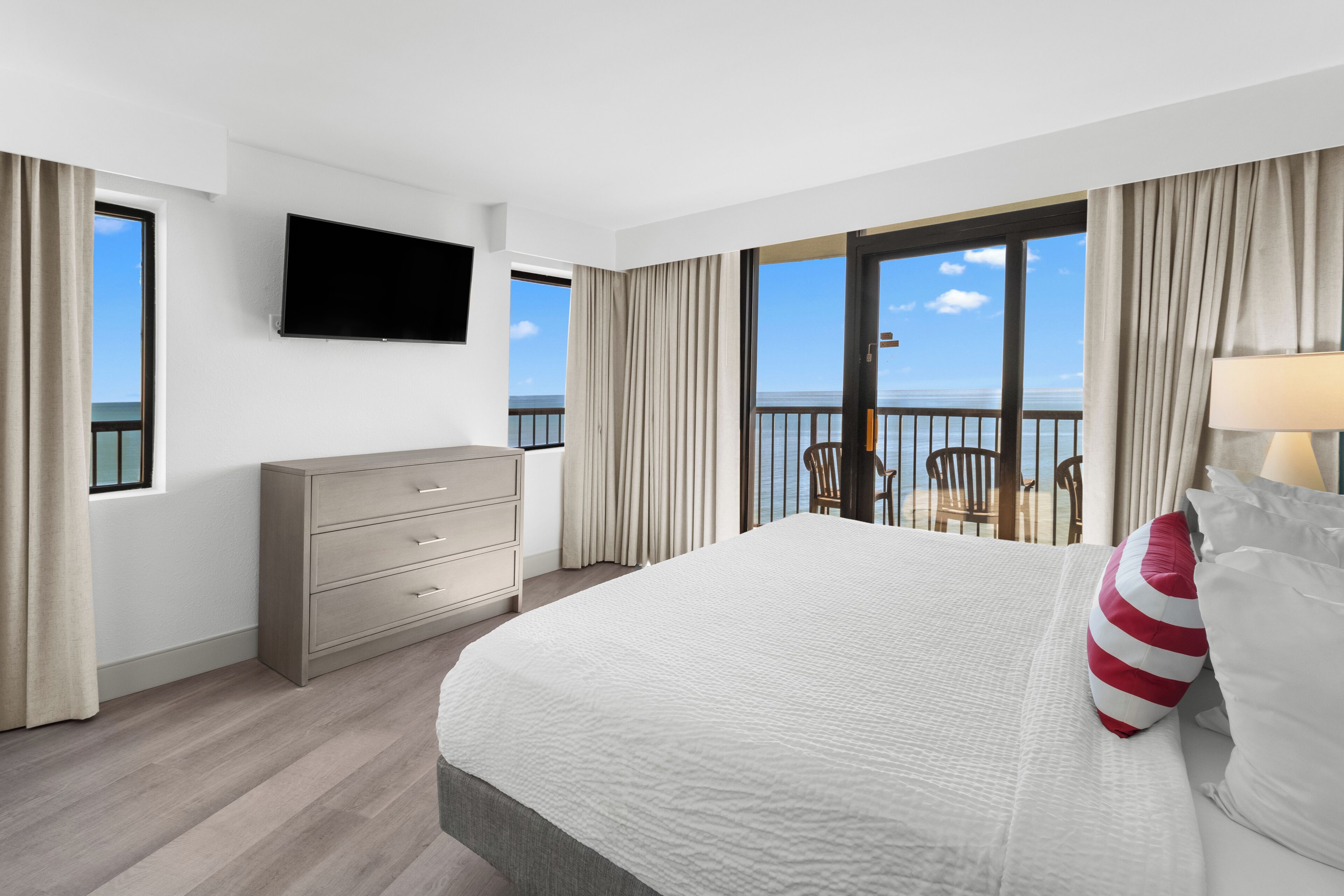 Camera d'albergo con un letto grande, una TV a parete, un comò e un balcone con vista sul mare.