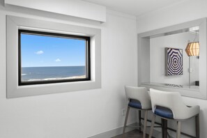 A modern room with a large window overlooking the sea, two bar stools, and a wall-mounted artwork.