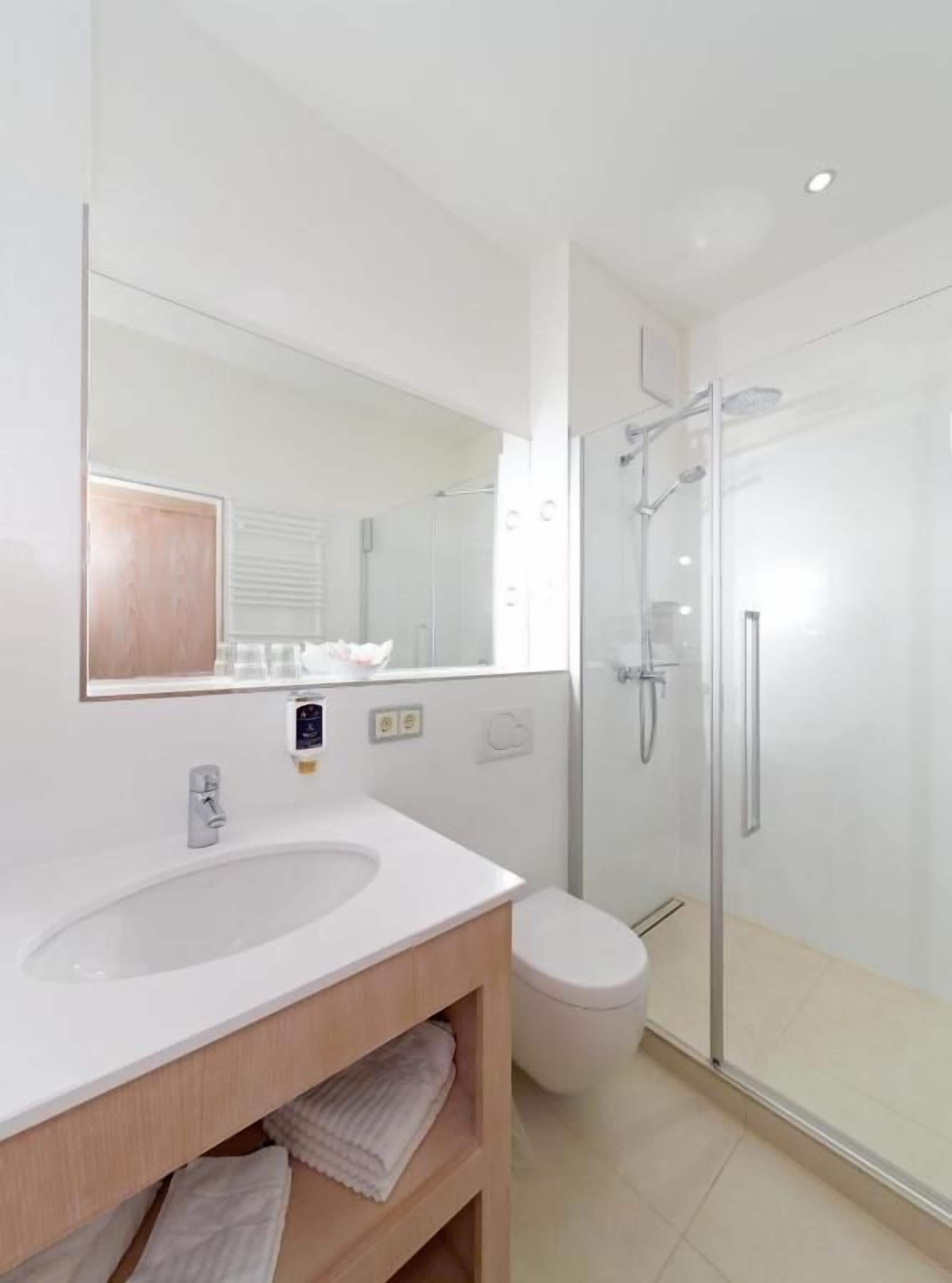 A modern bathroom with a white sink, mirror, and glass shower enclosure.