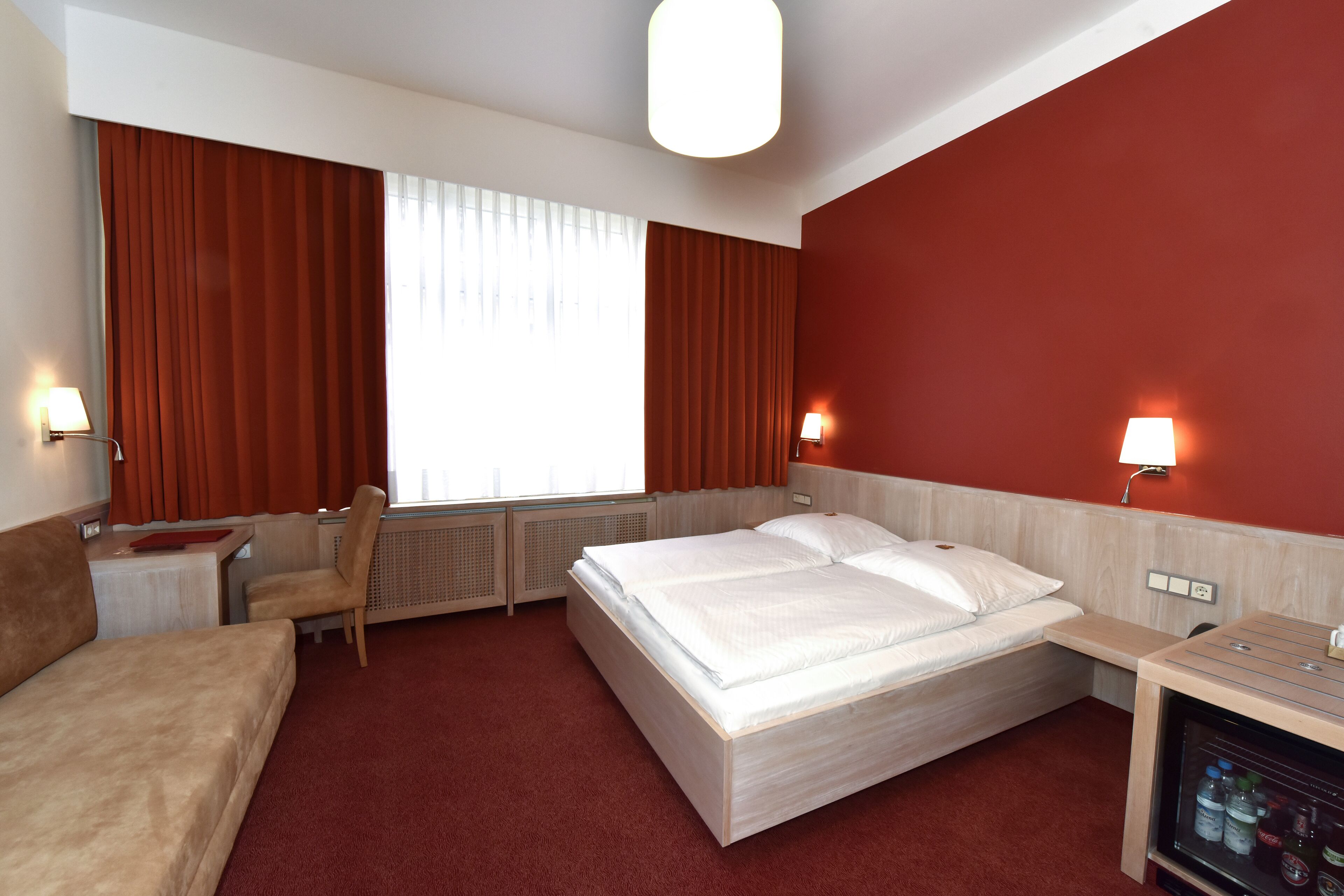 A hotel room with a bed, a desk, a chair, and a minibar.