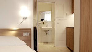 A hotel room with a bed, a bathroom with a sink and mirror, and a wooden cabinet. - Hotel ADRIA München (Munich)