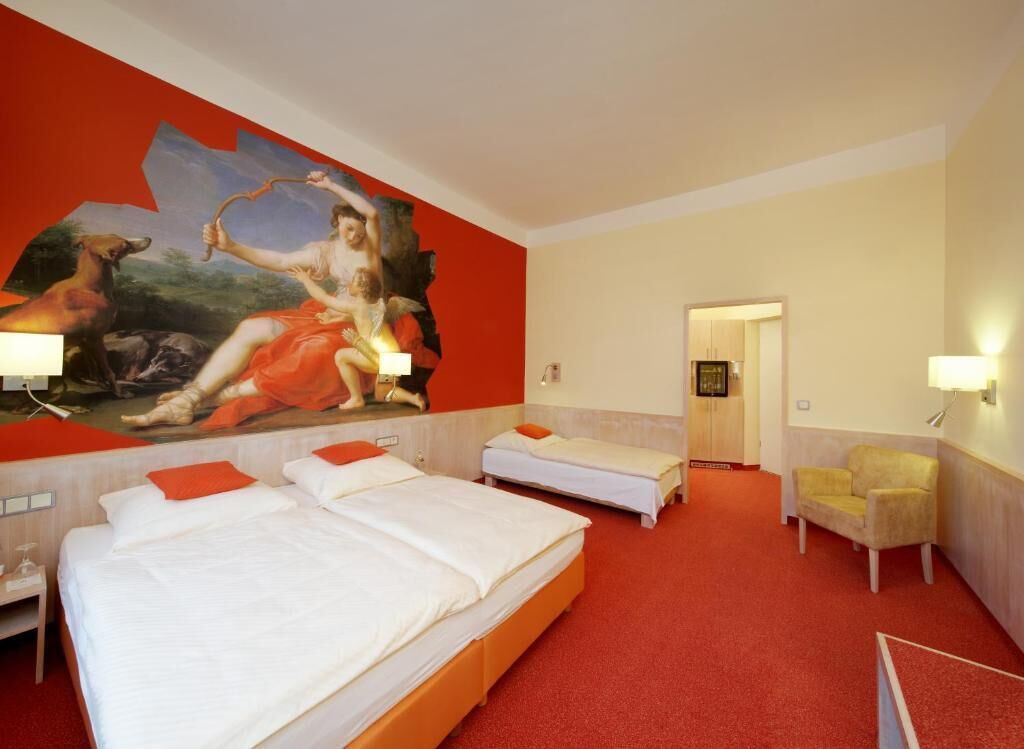 A hotel room with two beds, a large mural on the wall, a red carpet, and a chair.