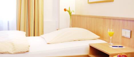 A hotel room with a bed, a bedside table with a glass of orange juice, a vase with a flower, and a basket of fruit.