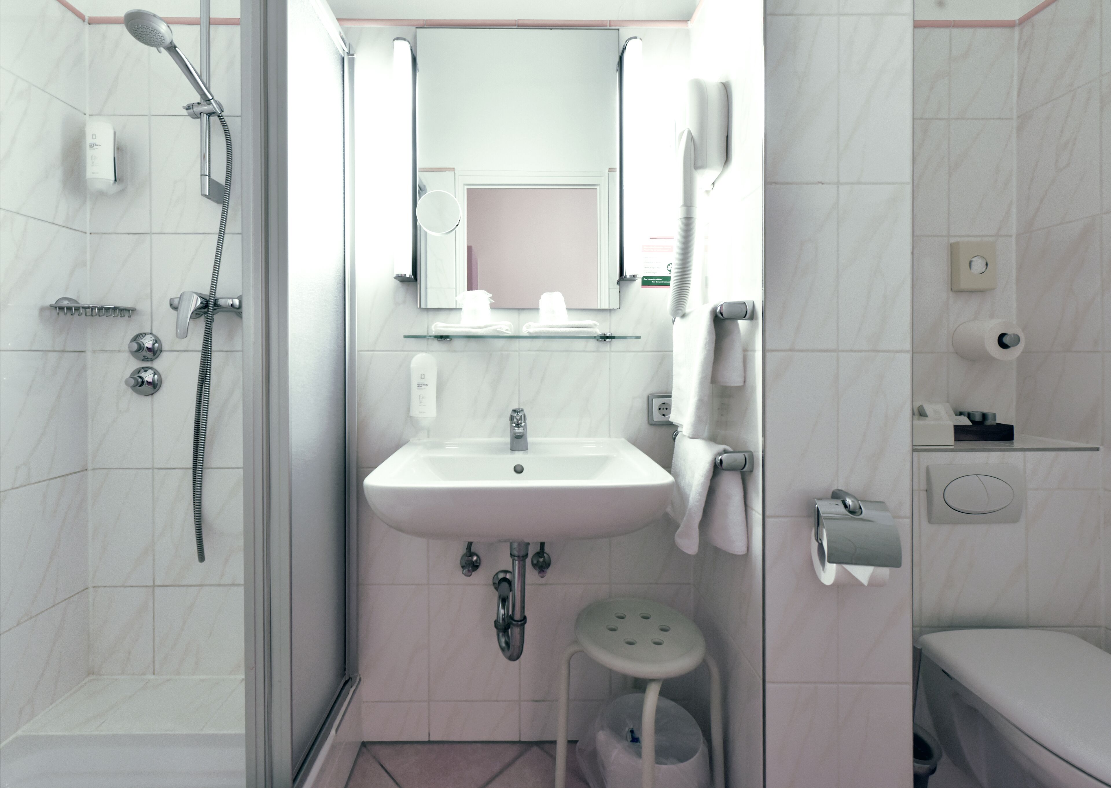 A modern bathroom with a shower, sink, toilet, and a small stool.