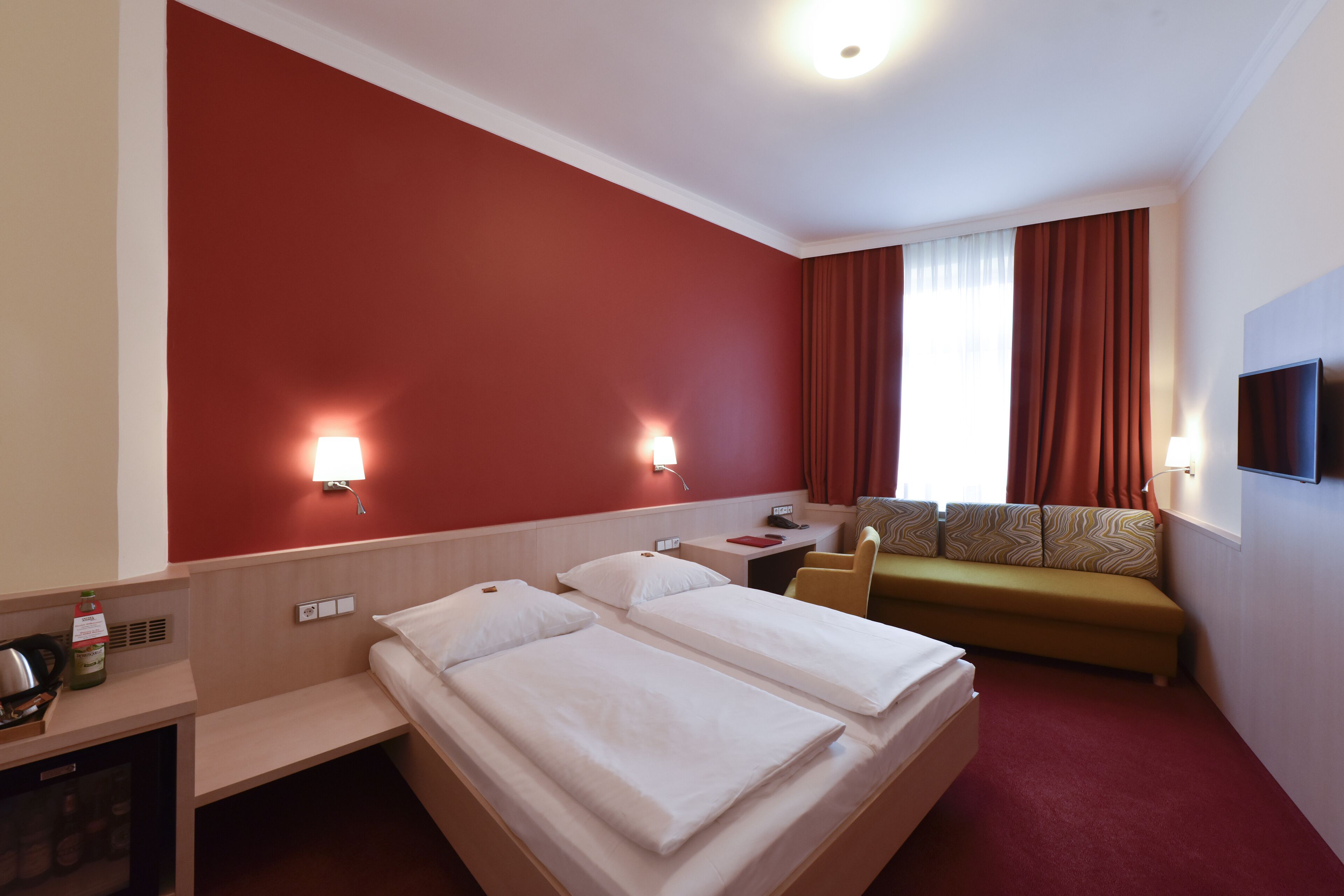 A hotel room with two beds, a desk with a telephone, a sofa, and a TV.