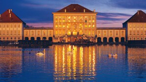 A large, illuminated building with multiple windows and a reflection in the water. - Hotel ADRIA München (Munich)