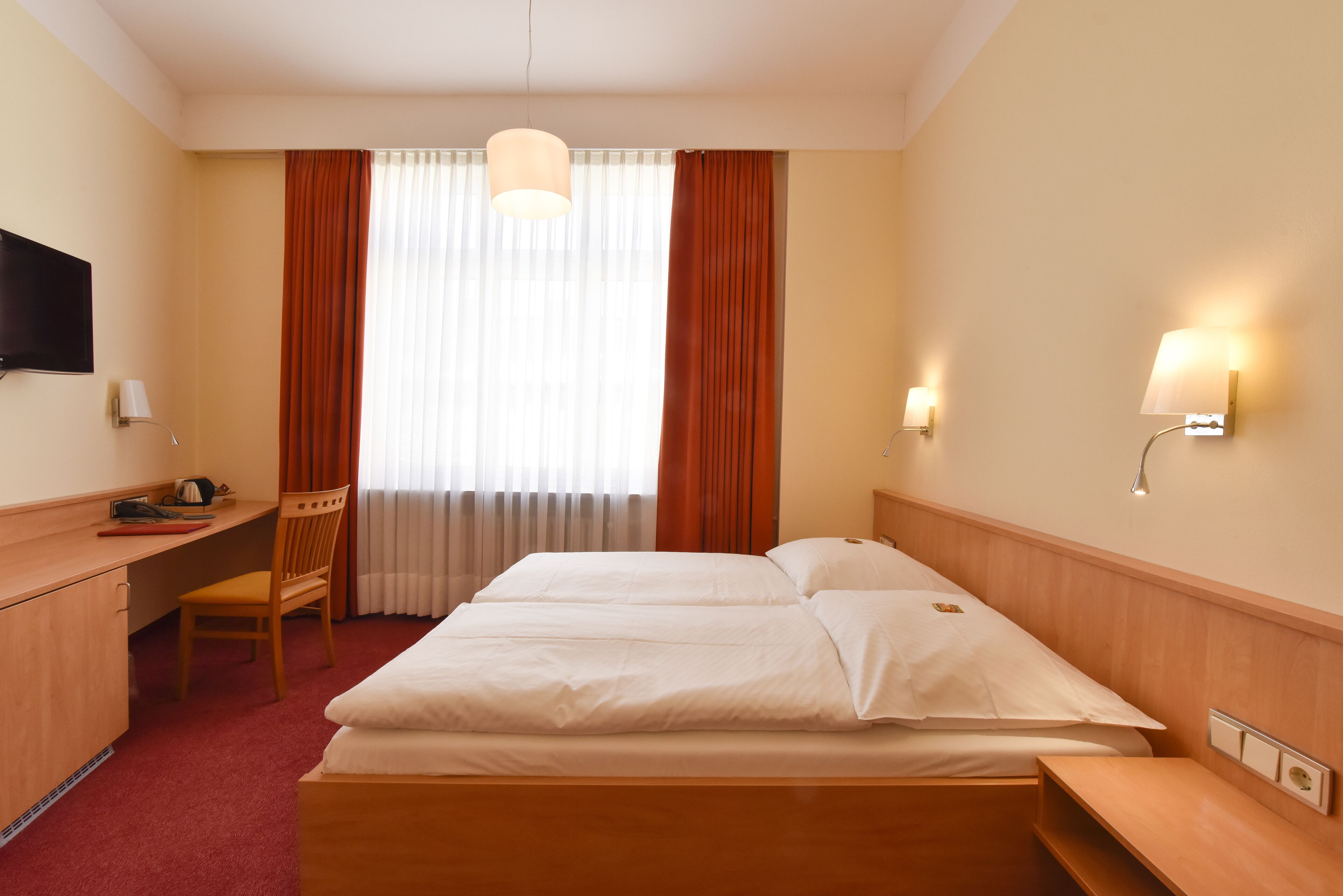 A hotel room with a bed, desk, chair, and a TV.