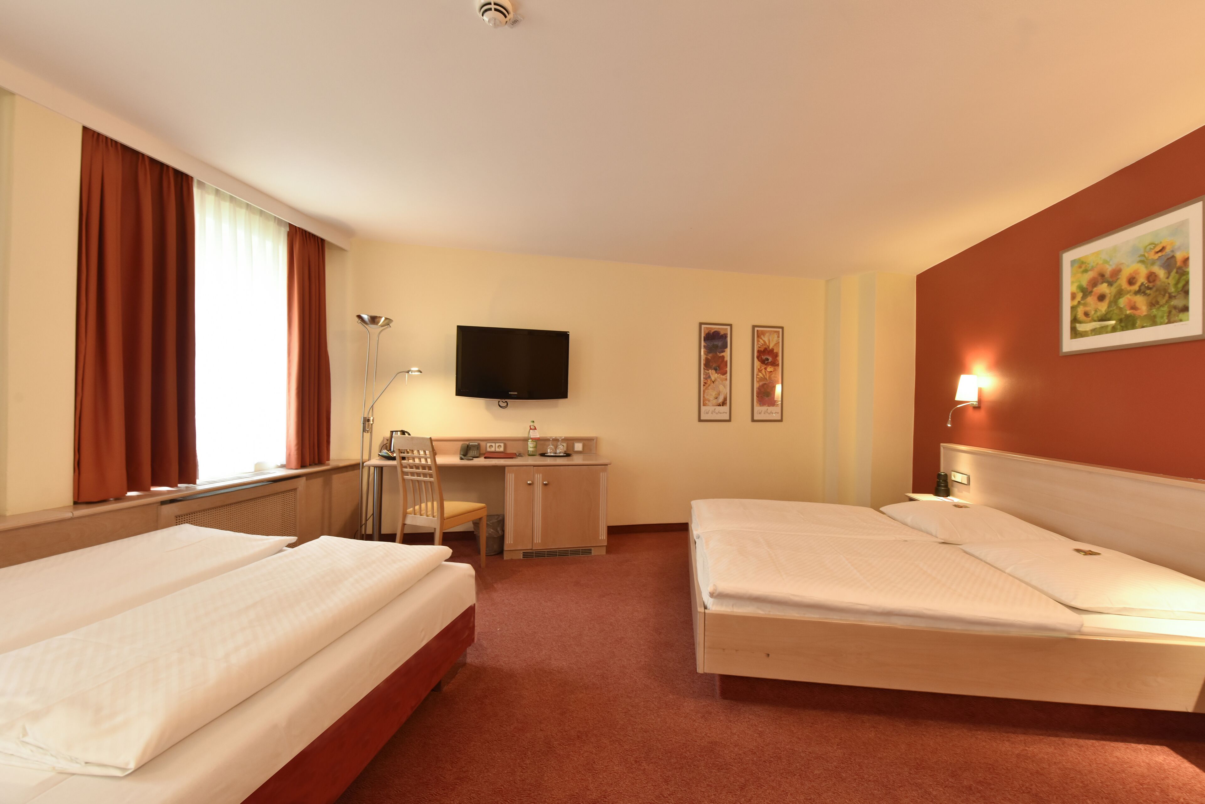 A hotel room with two beds, a desk, a chair, a TV, and a painting on the wall.