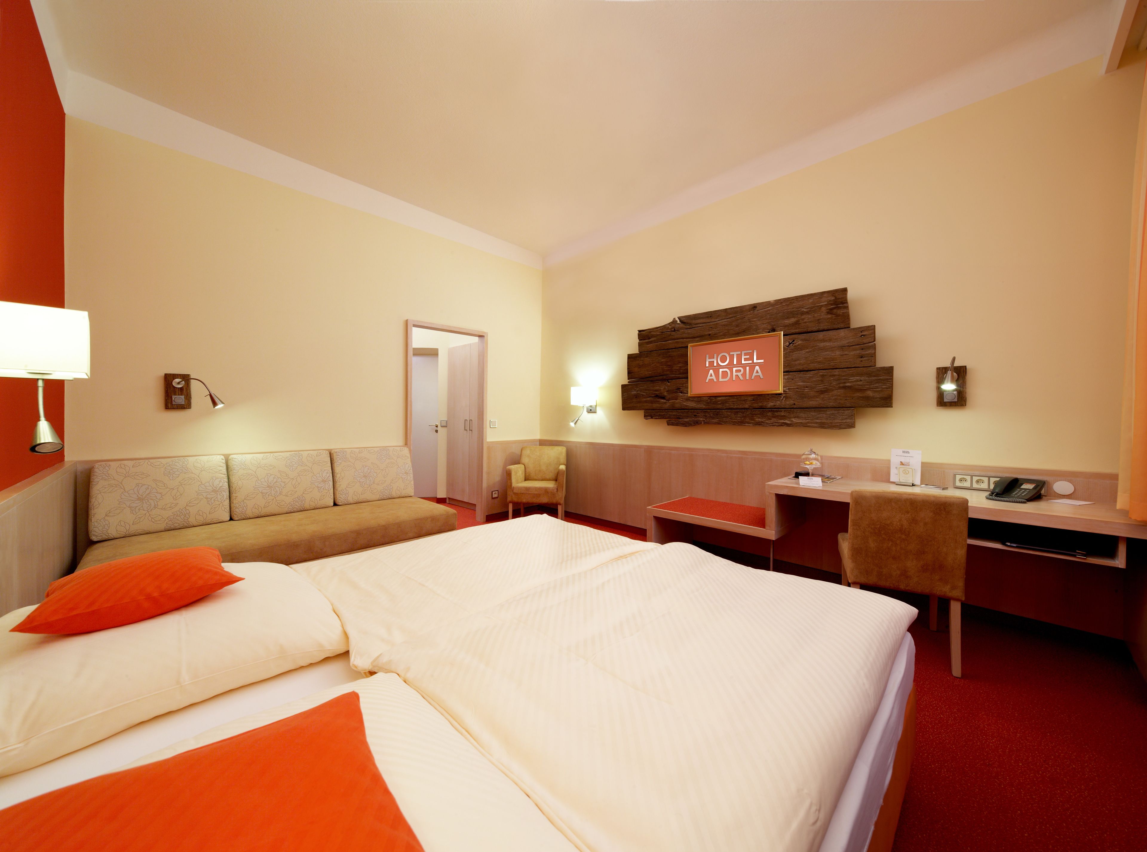 Ein Hotelzimmer mit einem großen Bett, einem Schreibtisch, einem Sessel, einer Couch und einer Tür zu einem weiteren Raum.
