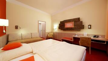 Ein Hotelzimmer mit einem großen Bett, einem Schreibtisch, einem Sessel, einer Couch und einer Tür zu einem weiteren Raum.