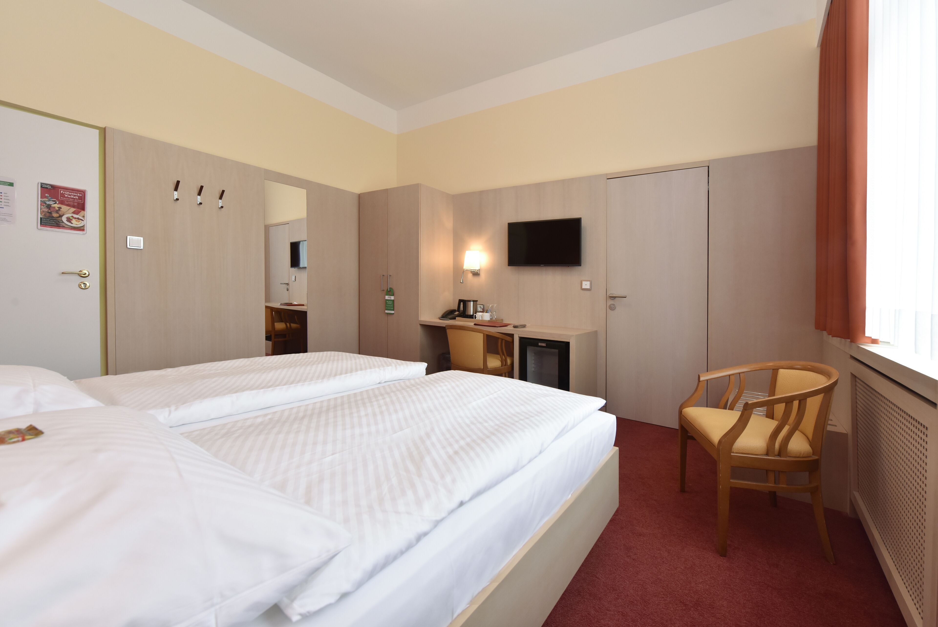 Una habitación de hotel con dos camas individuales, un escritorio con silla, televisión y espejo.