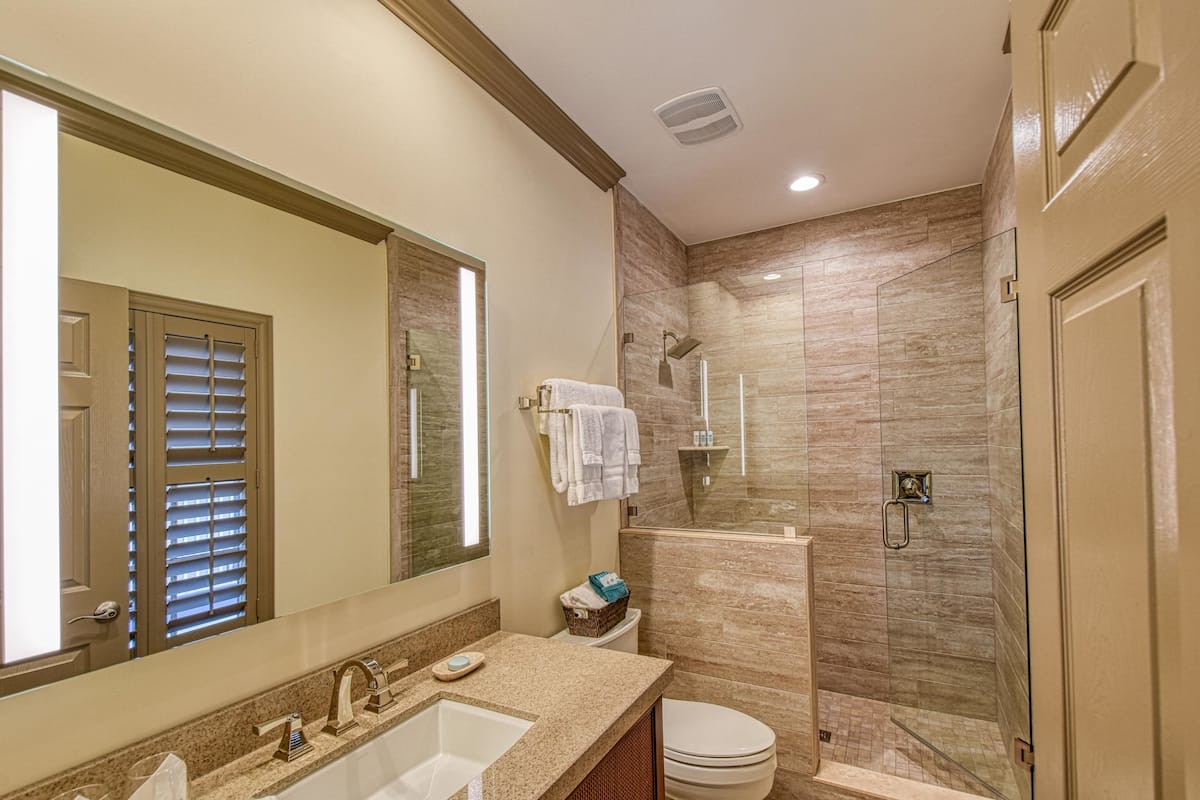 A modern bathroom with a large mirror, a sink, a toilet, and a glass-enclosed shower area.