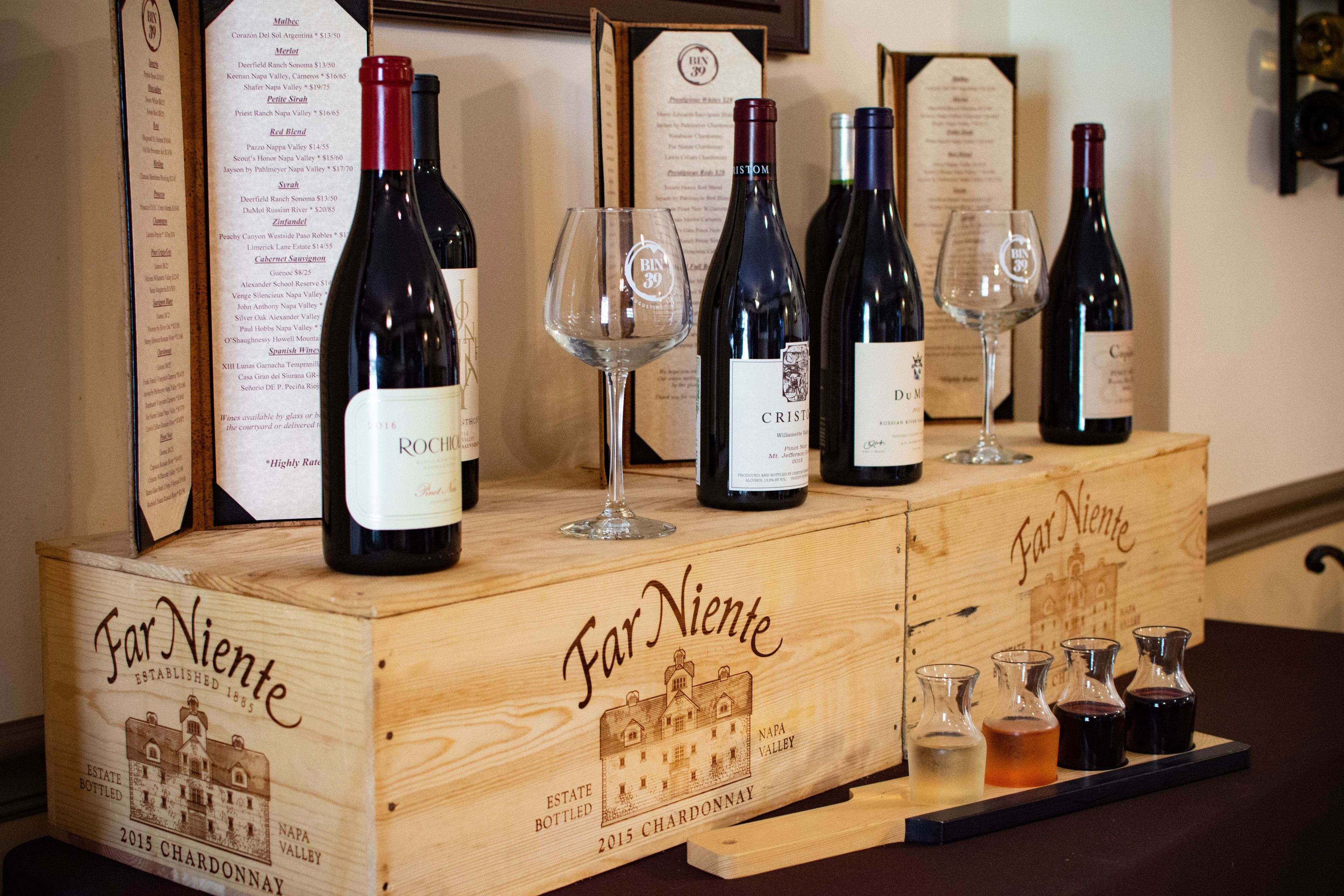A wooden crate labeled "Far Niente" with wine bottles and glasses on top, and a menu board in the background.