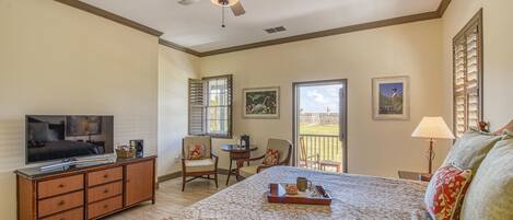 A bedroom with a bed, a television, a ceiling fan, a window, and a balcony.
