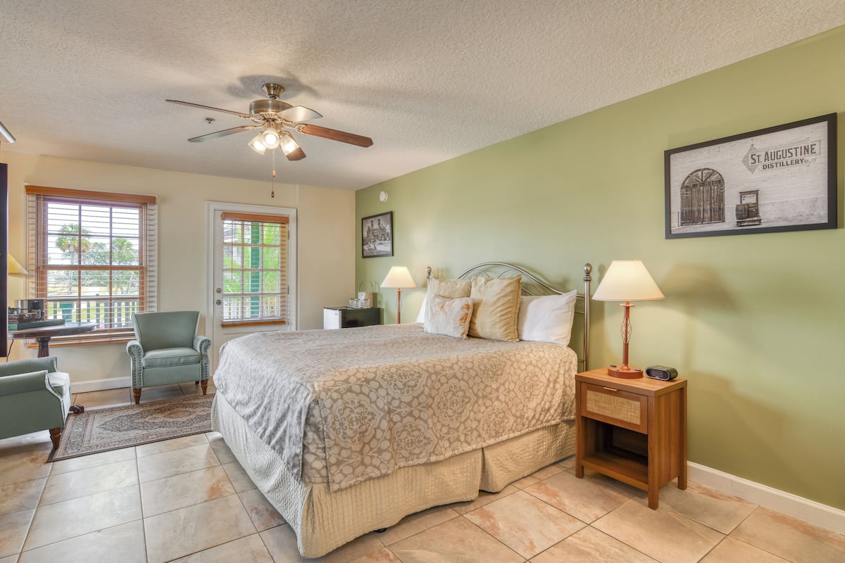 A bedroom with a bed, two bedside lamps, a nightstand, a chair, a desk, and a ceiling fan.