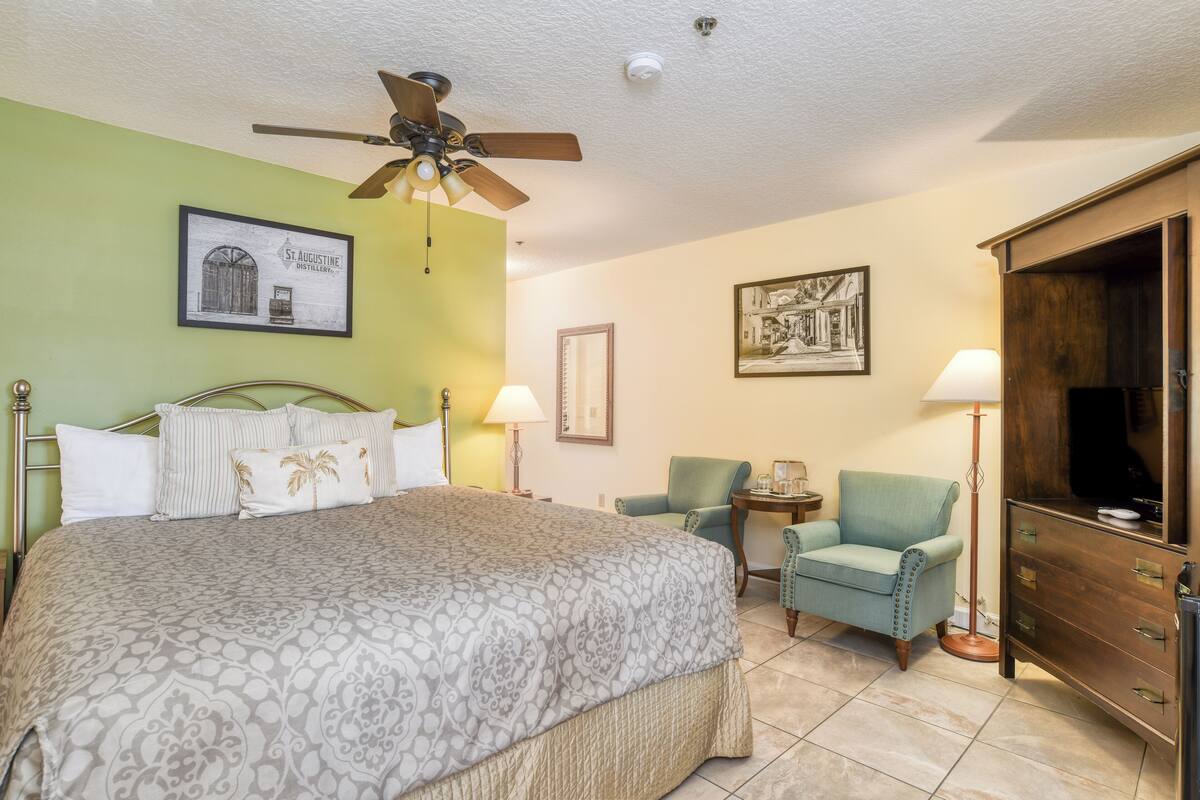 A hotel room with a bed, two chairs, a TV, and a wooden cabinet.