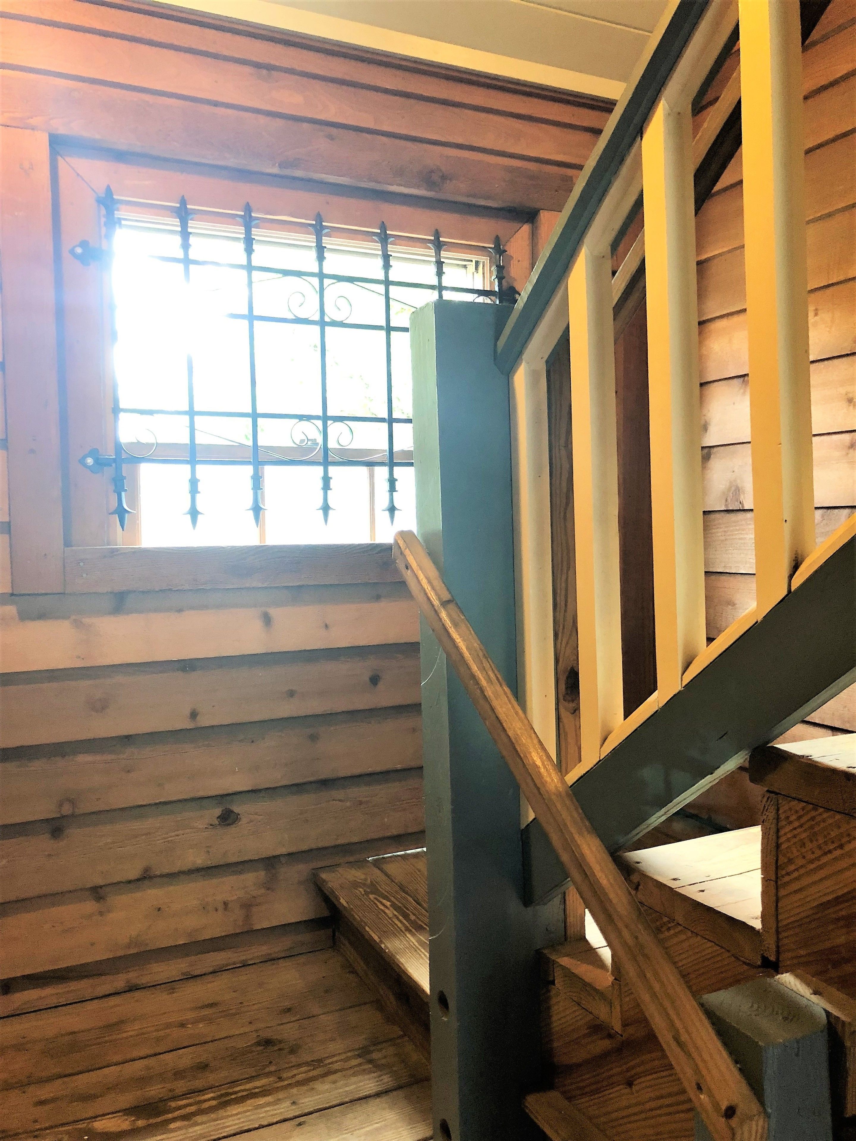 A wooden staircase with a metal railing and a window with bars.
