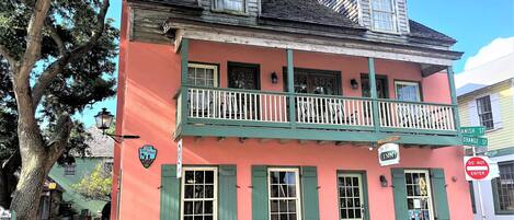 A two-story building with a balcony, green shutters, and a sign indicating 'City of Charleston Historic District'.
