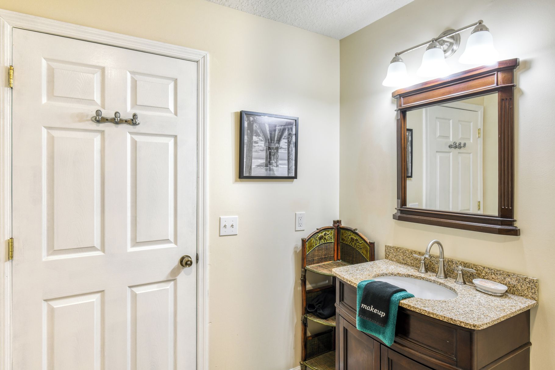 A bathroom with a white door, a framed picture on the wall, a vanity with a sink, and a mirror above the vanity.