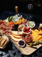 Un tagliere con salumi, formaggi, frutta e un bicchiere di vino su un tavolo in metallo.
