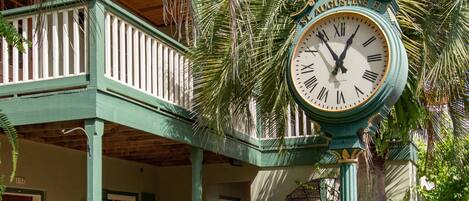 A clock with "St. Augustine FL" on it, set in a garden with a porch and palm trees.