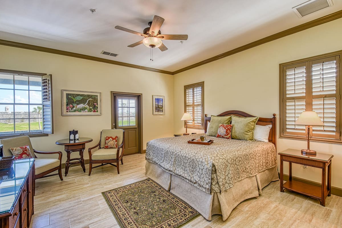 A bedroom with a bed, two nightstands, a chair, a table, and a ceiling fan.