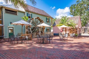 A courtyard with outdoor seating, a water wheel, and a building with a sign reading "Mule Shoe Tavern". - St George Inn (St. Augustine)