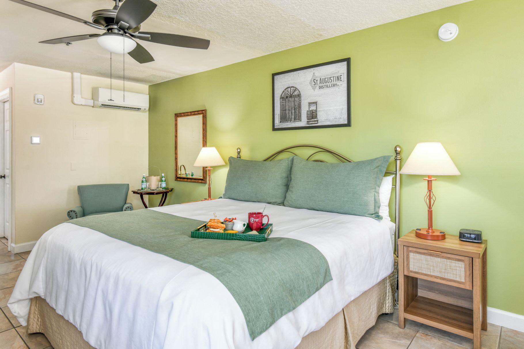 A hotel room with a bed, two bedside lamps, a ceiling fan, and a framed picture on the wall.