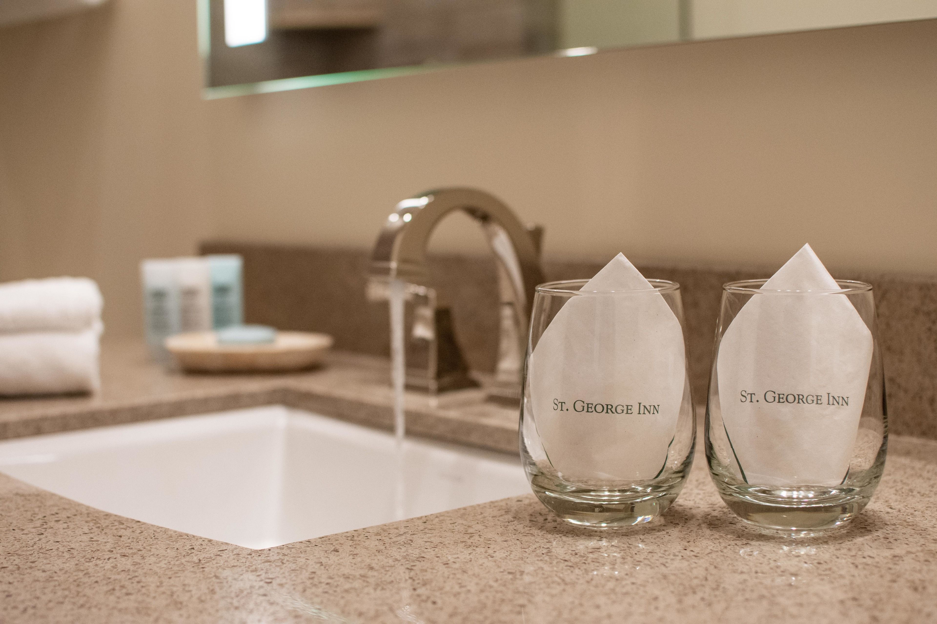 Zwei Gläser Wasser vom St. George Inn auf einer Arbeitsplatte mit Waschbecken und Spiegel im Hintergrund.
