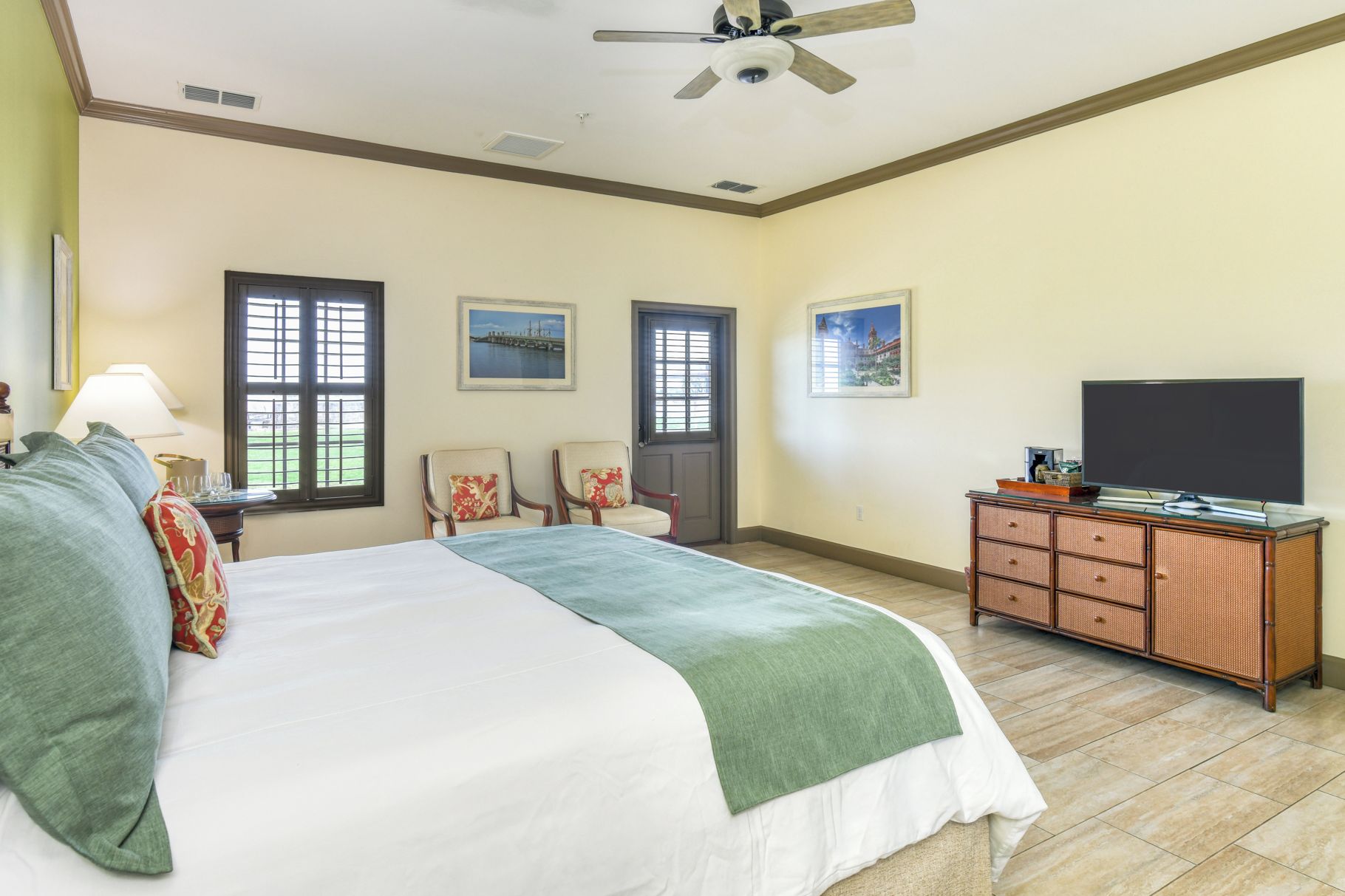 A hotel room with a bed, two chairs, a television, and artwork on the walls.