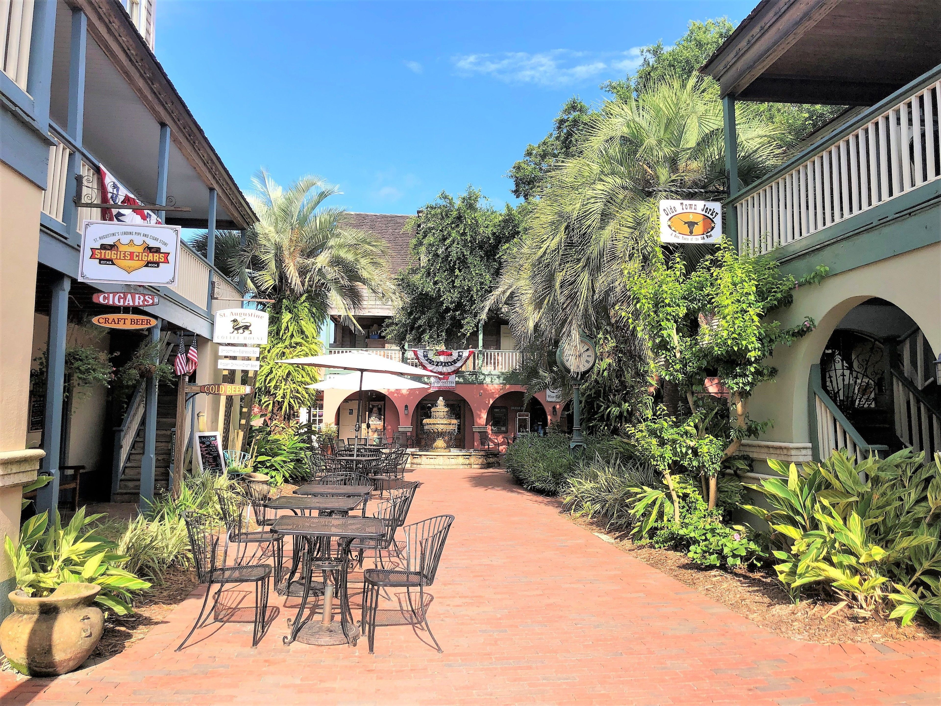 A courtyard with outdoor seating, a clock, and various signs for local businesses.