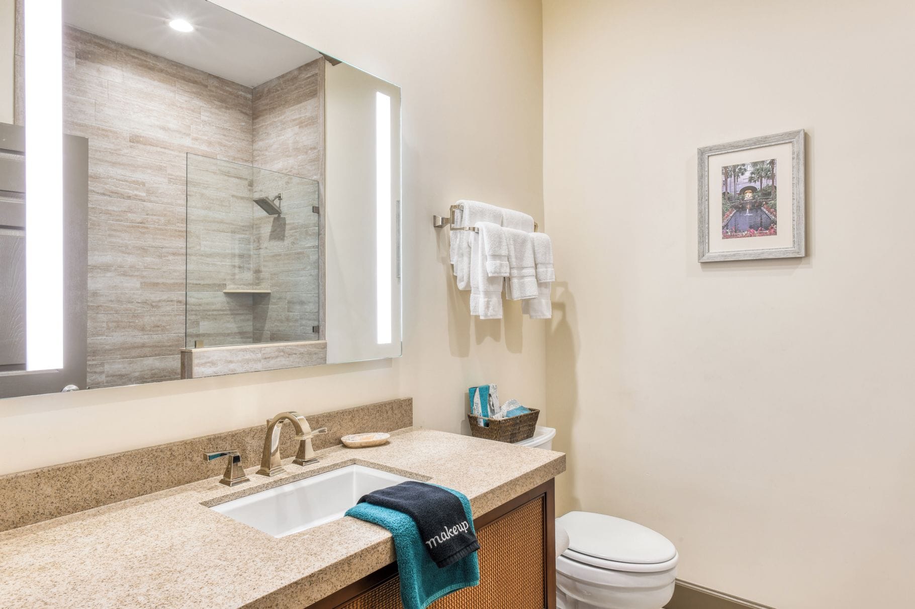 Une salle de bain équipée d’un lavabo, d’un miroir, d’un porte-serviettes et d’un tableau encadré au mur.