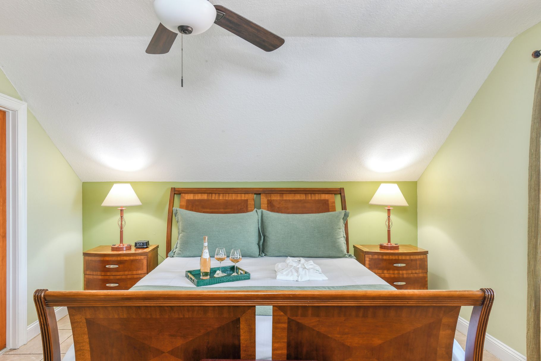 A bedroom with a bed, two bedside tables, a ceiling fan, and two lamps.
