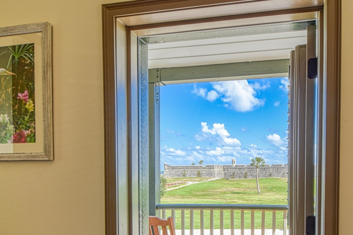 A view from a room through a glass door to an outdoor deck with a wooden chair and table.